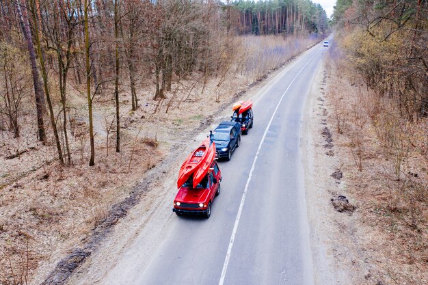 Varios autos con kayaks en la baca conduciendo en la carretera entre árboles