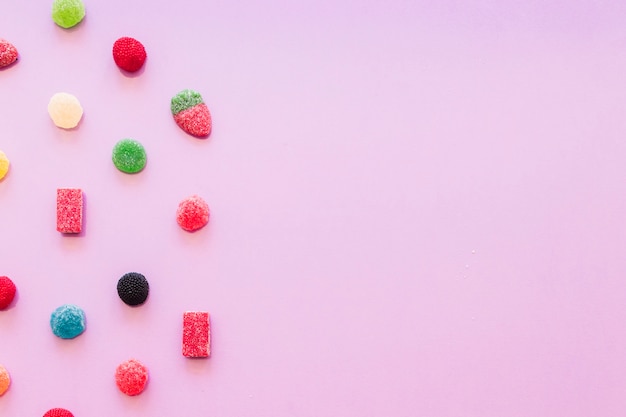 Varios caramelos de azúcar coloridos de la jalea en el papel pintado rosado