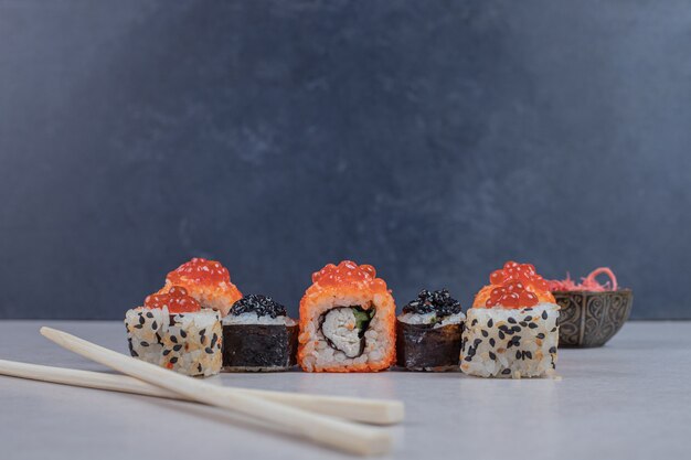 Varios rollos de sushi decorados con caviar rojo y palillos.
