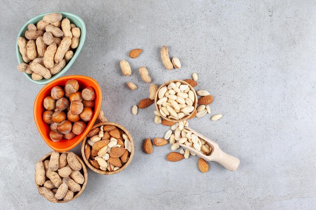 Varios tipos de nueces en tazones y esparcidas junto a primicia sobre fondo de mármol. Foto de alta calidad