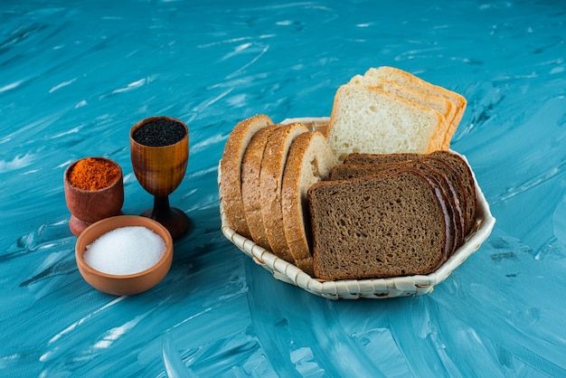 Varios tipos de pan fresco en una canasta con sal y pimienta sobre un fondo claro.