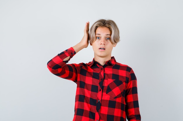 Varón adolescente rubio con la mano cerca de la oreja en camisa casual y mirando pensativo. vista frontal.