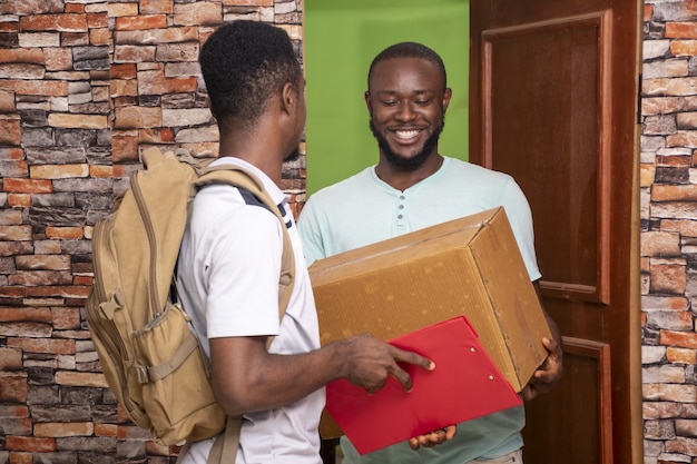 Varón africano recibiendo un paquete de un trabajador de servicio de entrega