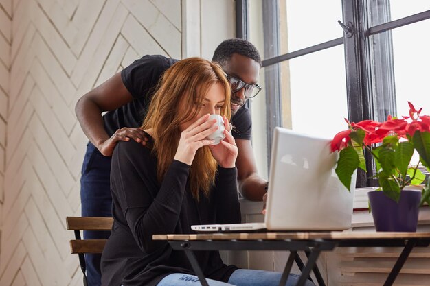 Varón afroamericano y mujer caucásica trabajando con una laptop en la mesa.