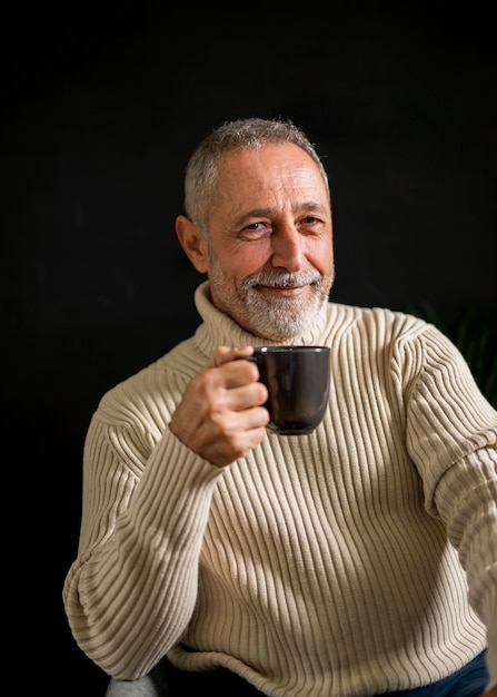 Varón anciano sonriente con bebida caliente