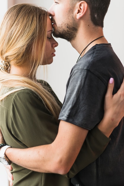 Varón cariñoso joven besando a su novia en la frente