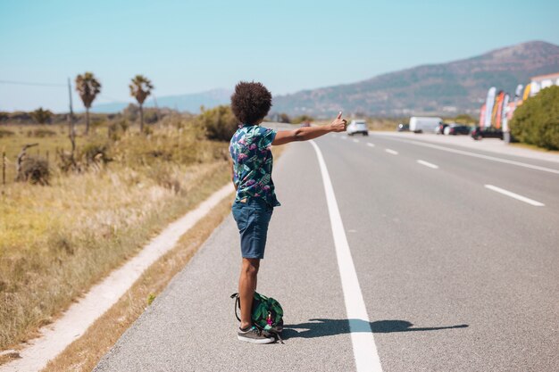 Varón étnico haciendo autostop en la carretera