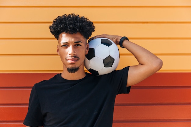 Varón étnico que sostiene el balón de fútbol en hombro