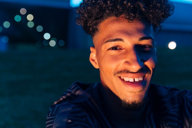 Varón étnico sonriente con el pelo rizado en la noche