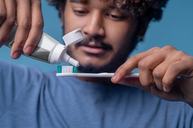 Varón indio enfocado exprimiendo la pasta de dientes de un tubo de plástico abierto en su cepillo de dientes