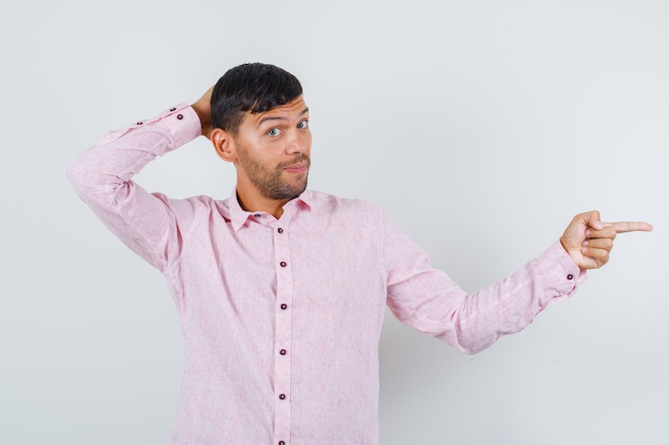 Foto gratuito varón joven apuntando al lado con la mano detrás de la cabeza en camisa rosa, vista frontal.