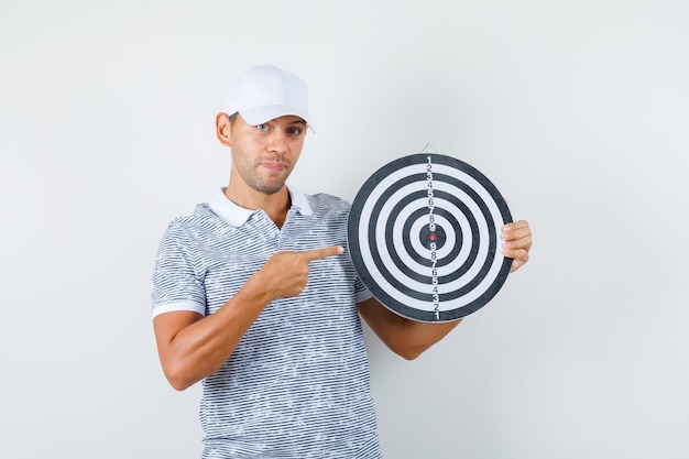 Foto gratuita varón joven apuntando al tablero de dardos en camiseta y gorra y mirando alegre