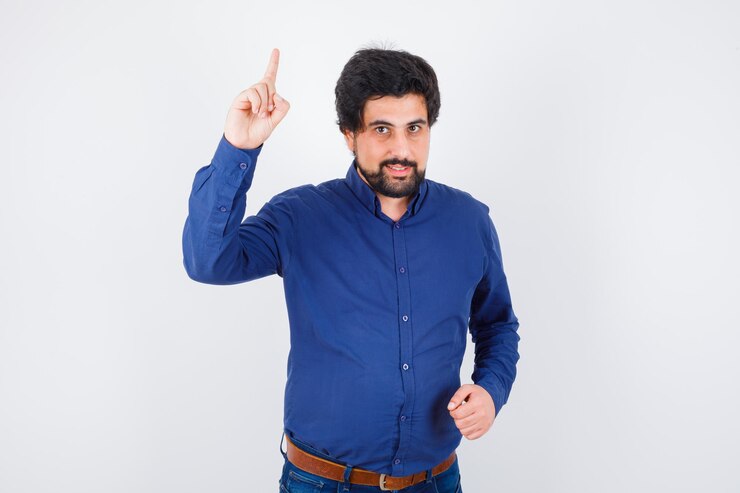 Foto gratuito varón joven apuntando hacia arriba con camisa azul real y mirando atento. vista frontal.