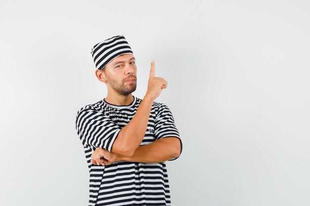 Varón joven apuntando hacia arriba con sombrero de camiseta a rayas y mirando confiado
