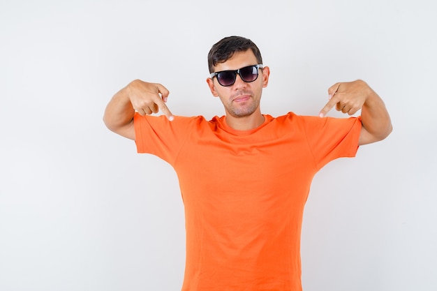 Varón joven apuntando con el dedo hacia abajo en camiseta naranja y mirando confiado