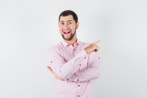 Varón joven apuntando hacia fuera en camisa rosa y mirando alegre