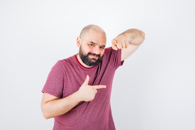 Foto gratuita varón joven apuntando a un lado y a la cámara en camiseta rosa, vista frontal.