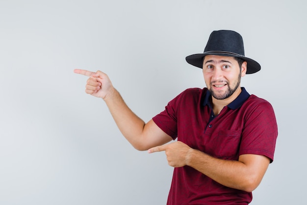 Foto gratuita varón joven apuntando a un lado en camiseta, sombrero y mirando enfocado, vista frontal.