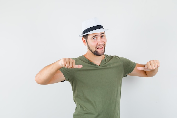 Foto gratuito varón joven apuntando los pulgares a sí mismo en camiseta verde y sombrero y luciendo bien