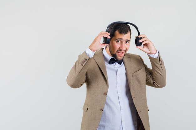 Varón joven con auriculares en traje y mirando confiado. vista frontal.