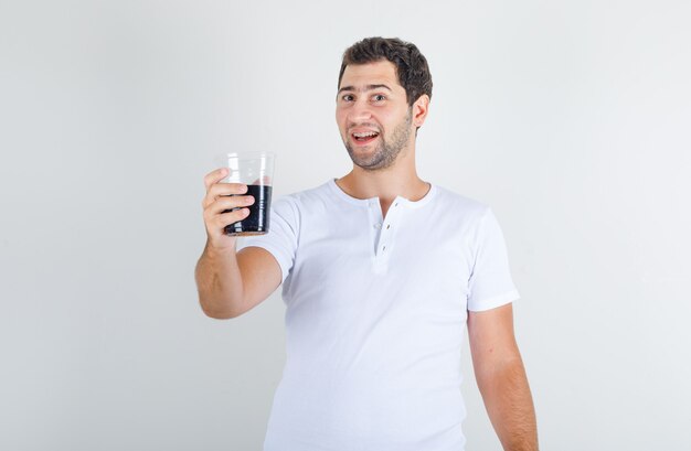 Varón joven con bebida de cola en camiseta blanca y mirando feliz