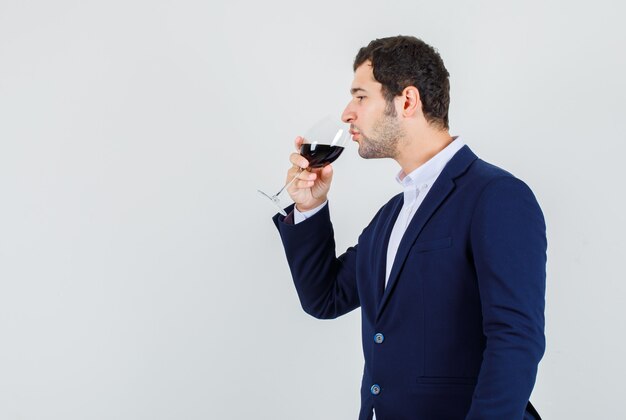 Varón joven bebiendo alcohol en traje azul oscuro y buscando pacífica.