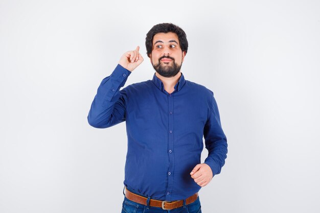 Varón joven en camisa azul real apuntando hacia atrás y mirando atenta, vista frontal.