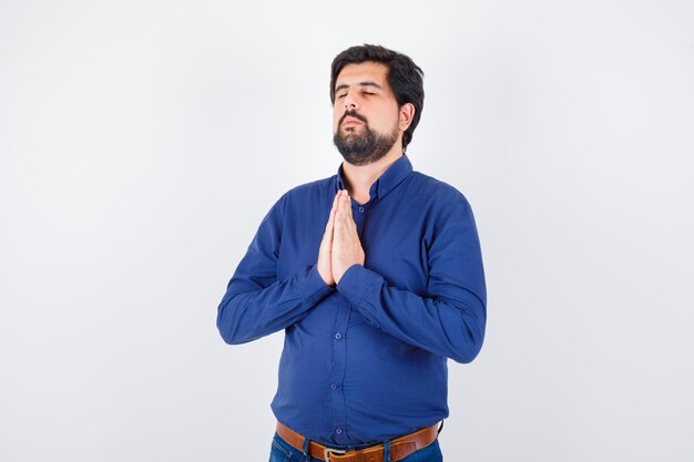 Varón joven en camisa azul real deseando y mirando esperanzado, vista frontal.