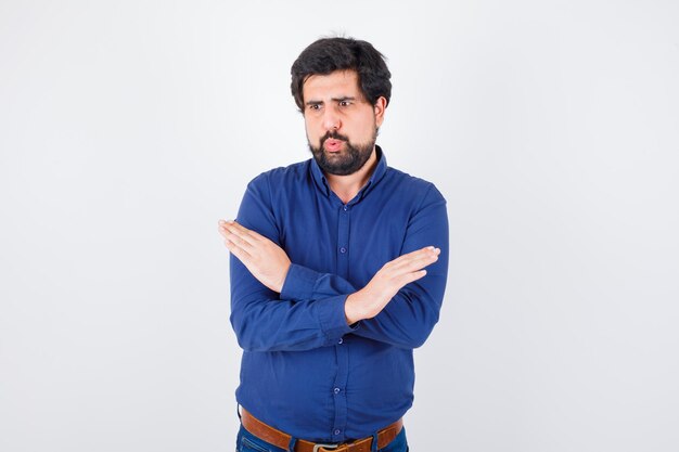 Varón joven en camisa azul real que muestra gesto cerrado, vista frontal.