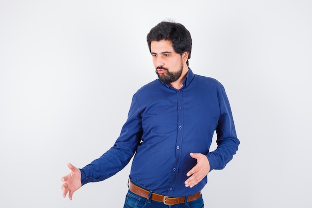 Varón joven en camisa azul real que muestra el tamaño de algo, vista frontal.