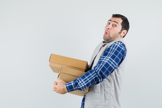 Foto gratuita varón joven en camisa, chaqueta llevando cajas y mirando duro, vista frontal.