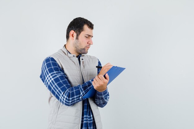 Varón joven en camisa, chaqueta notando algo en el papel y mirando concentrado