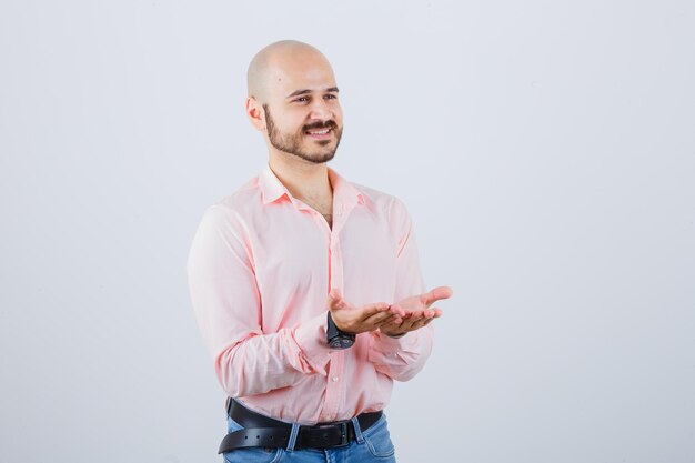 Varón joven en camisa, jeans estirando las manos ahuecadas y mirando pacífica, vista frontal.