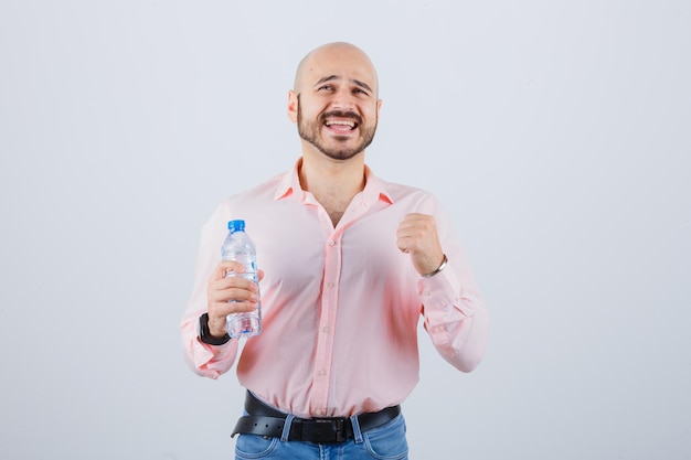 Varón joven en camisa, jeans mostrando gesto de ganador y con suerte, vista frontal.