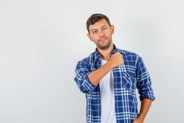 Varón joven en camisa posando mostrando el puño cerrado del brazo y mirando confiado, vista frontal.