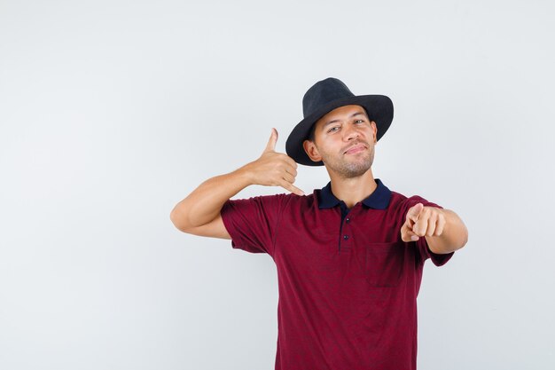 Varón joven con camisa roja, sombrero negro mostrando gesto de llamarme y mirando impaciente, vista frontal.