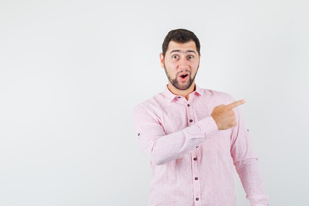 Varón joven en camisa rosa apuntando hacia un lado y mirando asombrado