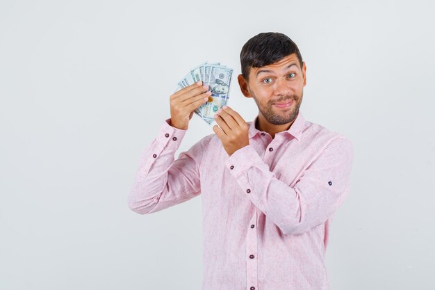 Foto gratuita varón joven en camisa rosa con billetes de un dólar y mirando alegre, vista frontal.