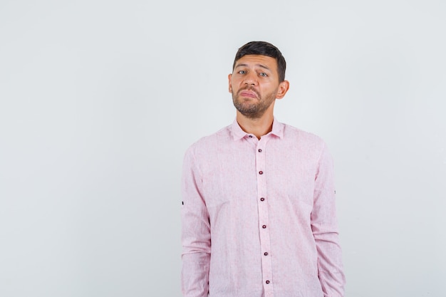 Foto gratuita varón joven en camisa rosa y mirando miserable, vista frontal.