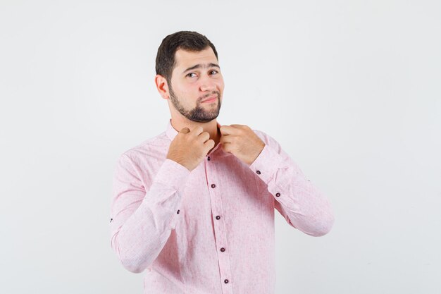 Varón joven en camisa rosa sosteniendo su cuello y mirando guapo