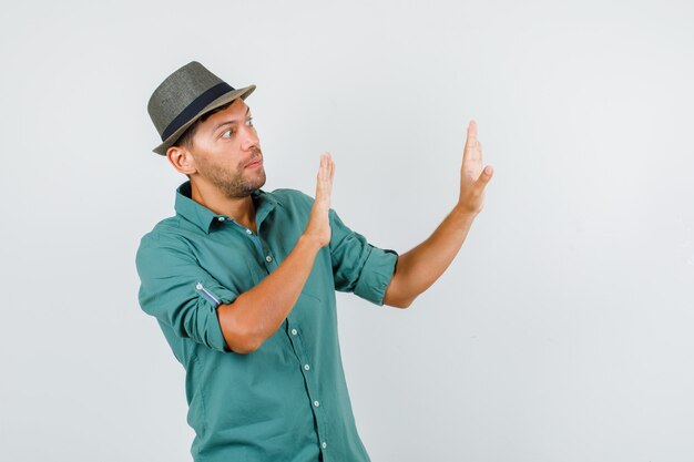 Varón joven en camisa, sombrero mostrando gesto de parada y mirando asustado