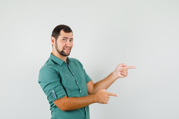 Varón joven en camisa verde apuntando a un lado y mirando positivo, vista frontal.