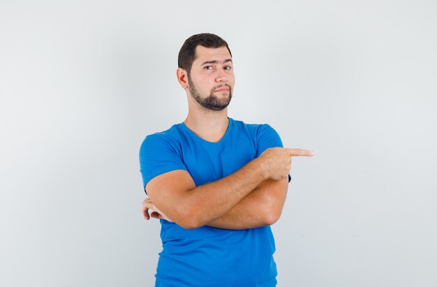 Varón joven en camiseta azul apuntando hacia un lado y mirando confiado