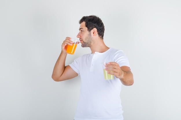 Varón joven en camiseta blanca bebiendo un vaso de jugo y mirando sediento