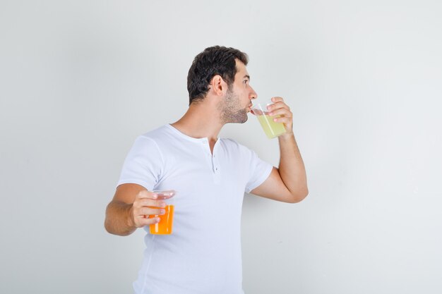 Varón joven en camiseta blanca bebiendo un vaso de jugo y mirando sediento