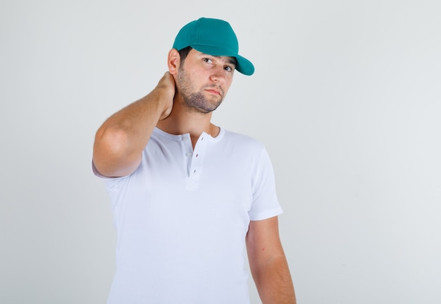 Varón joven en camiseta blanca con gorra posando con la mano en el cuello