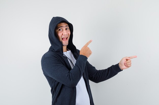 Varón joven en camiseta, chaqueta apuntando hacia el lado derecho y mirando feliz, vista frontal.