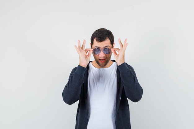 Foto gratuita varón joven en camiseta, chaqueta con gafas y mirando confiado, vista frontal.