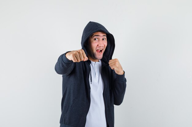 Varón joven en camiseta, chaqueta de pie en pose de lucha y mirando confiado, vista frontal.