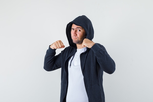 Varón joven en camiseta, chaqueta de pie en pose de lucha y mirando confiado, vista frontal.